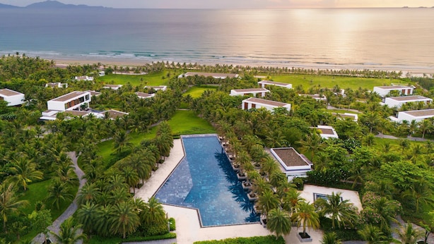 Un resort con una piscina central, varias villas para huéspedes y vista a la playa.