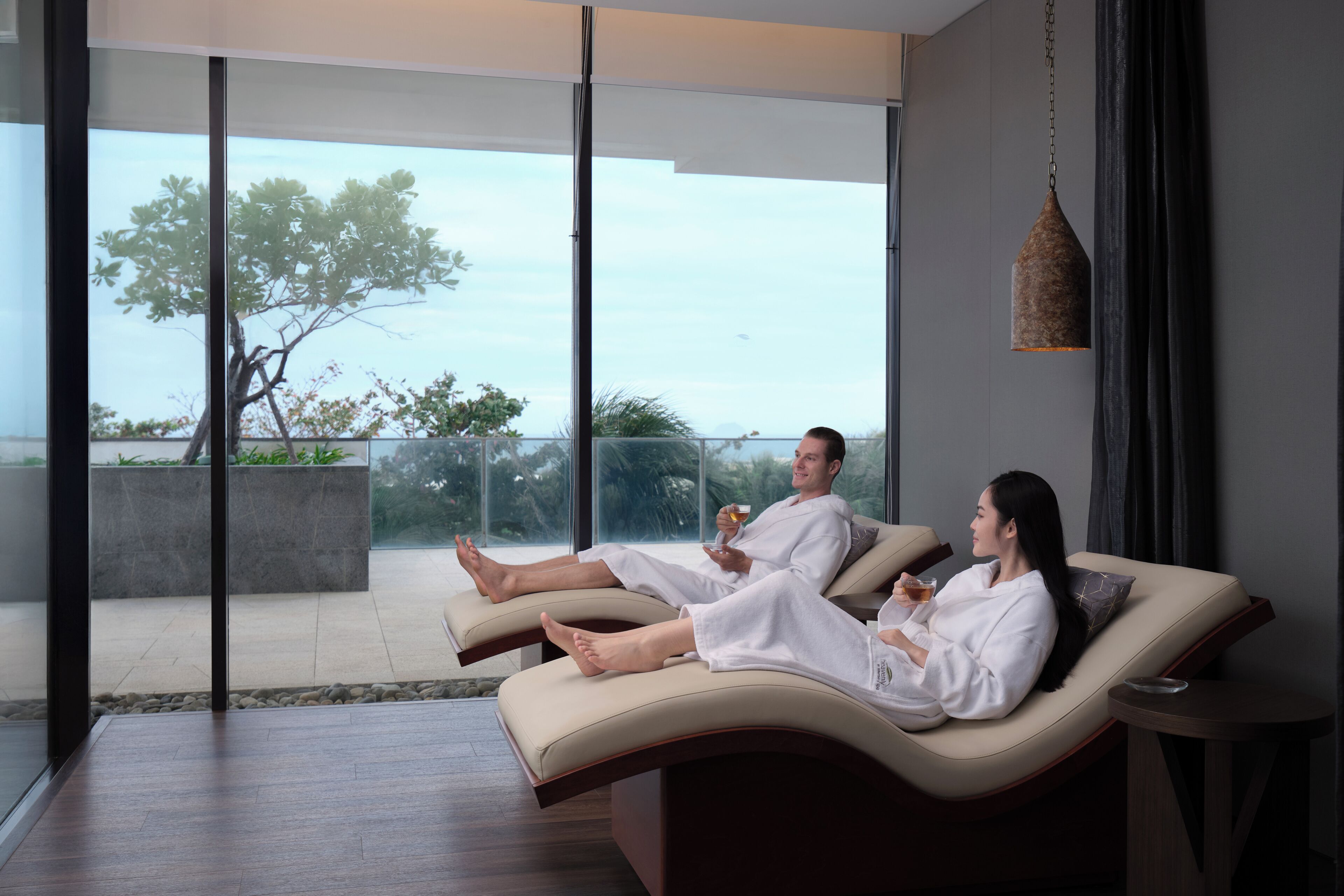 Dos personas descansando en una silla lounge curva, con vista a un balcón y al exterior.