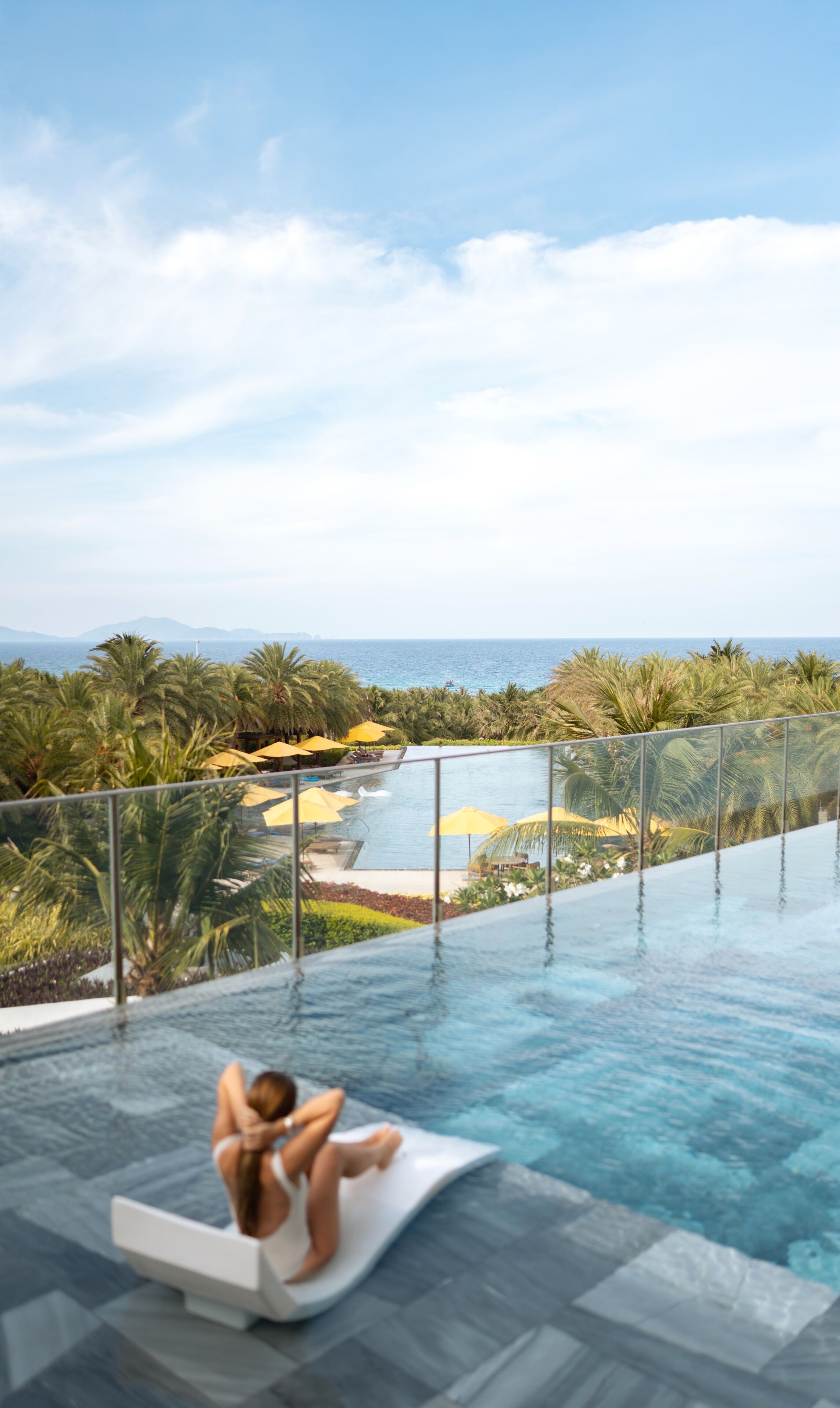 A person relaxing on a floating platform in a infinity pool overlooking a beach and ocean.