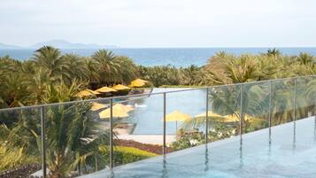 A person relaxing on a floating platform in a infinity pool overlooking a beach and ocean.