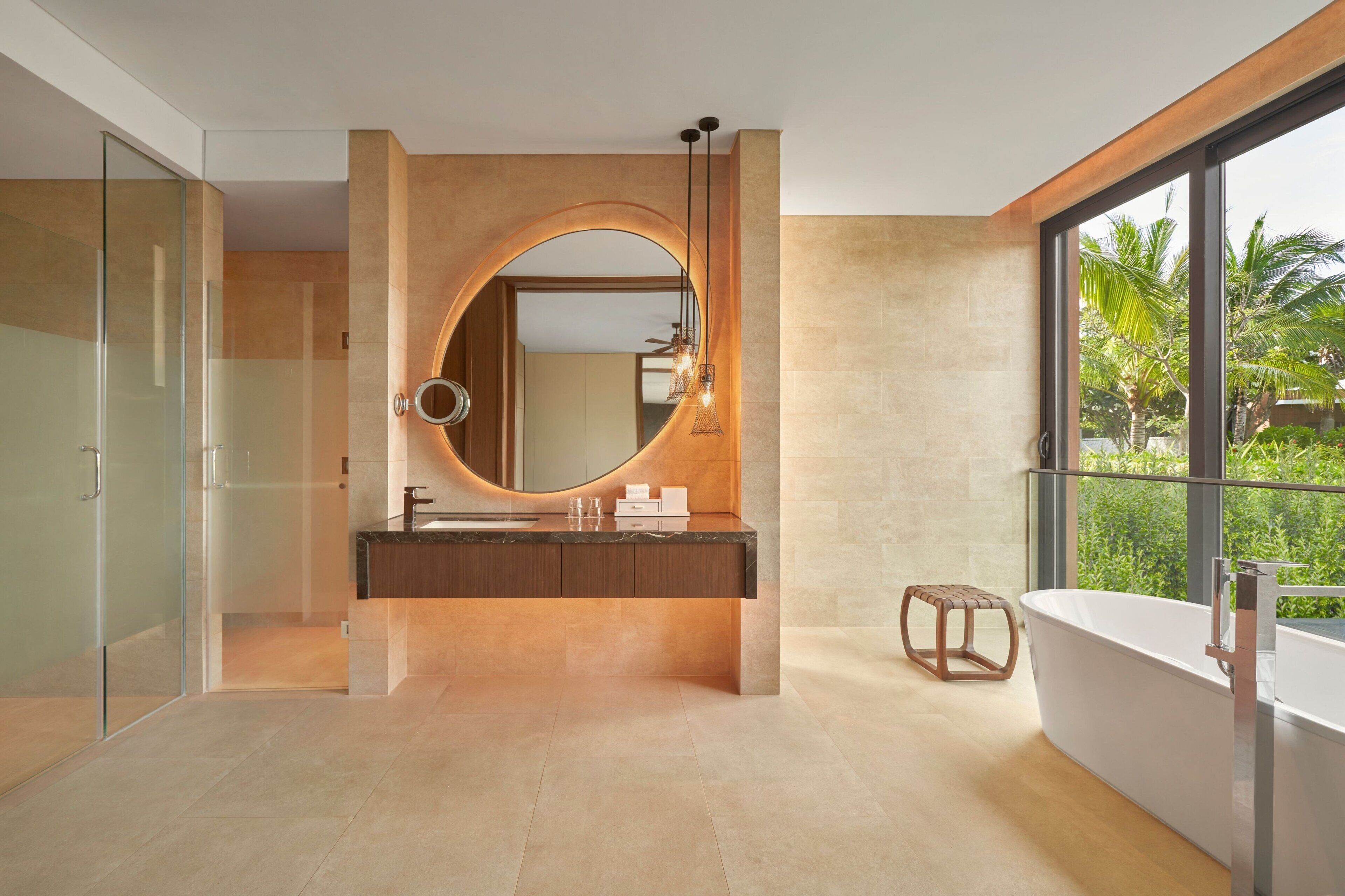 A modern bathroom with a large oval mirror, a freestanding bathtub, and a glass-enclosed shower area.