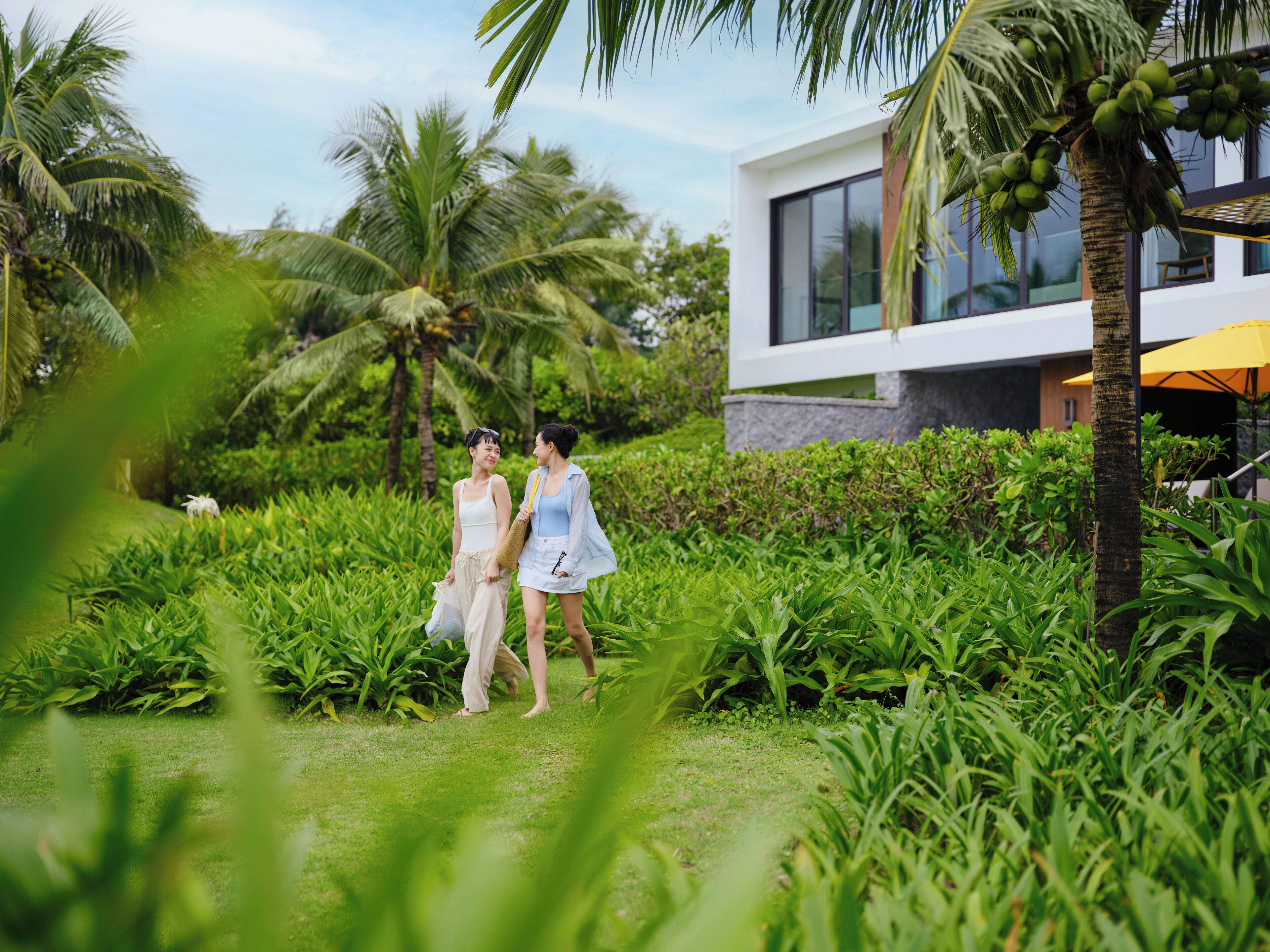 A lush garden with palm trees and a modern building with large windows.