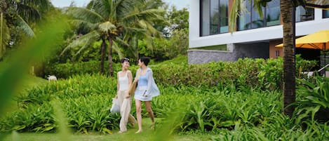 A lush garden with palm trees and a modern building with large windows.