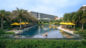 A swimming pool with lounge chairs and umbrellas, surrounded by palm trees and a modern building in the background. - The Westin Resort & Spa Cam Ranh (Cam Lam)