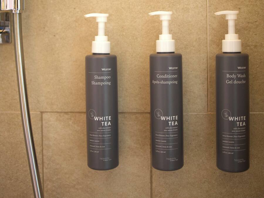 Casa de banho com chuveiro, três frascos de champô, condicionador e gel de banho Westin White Tea.