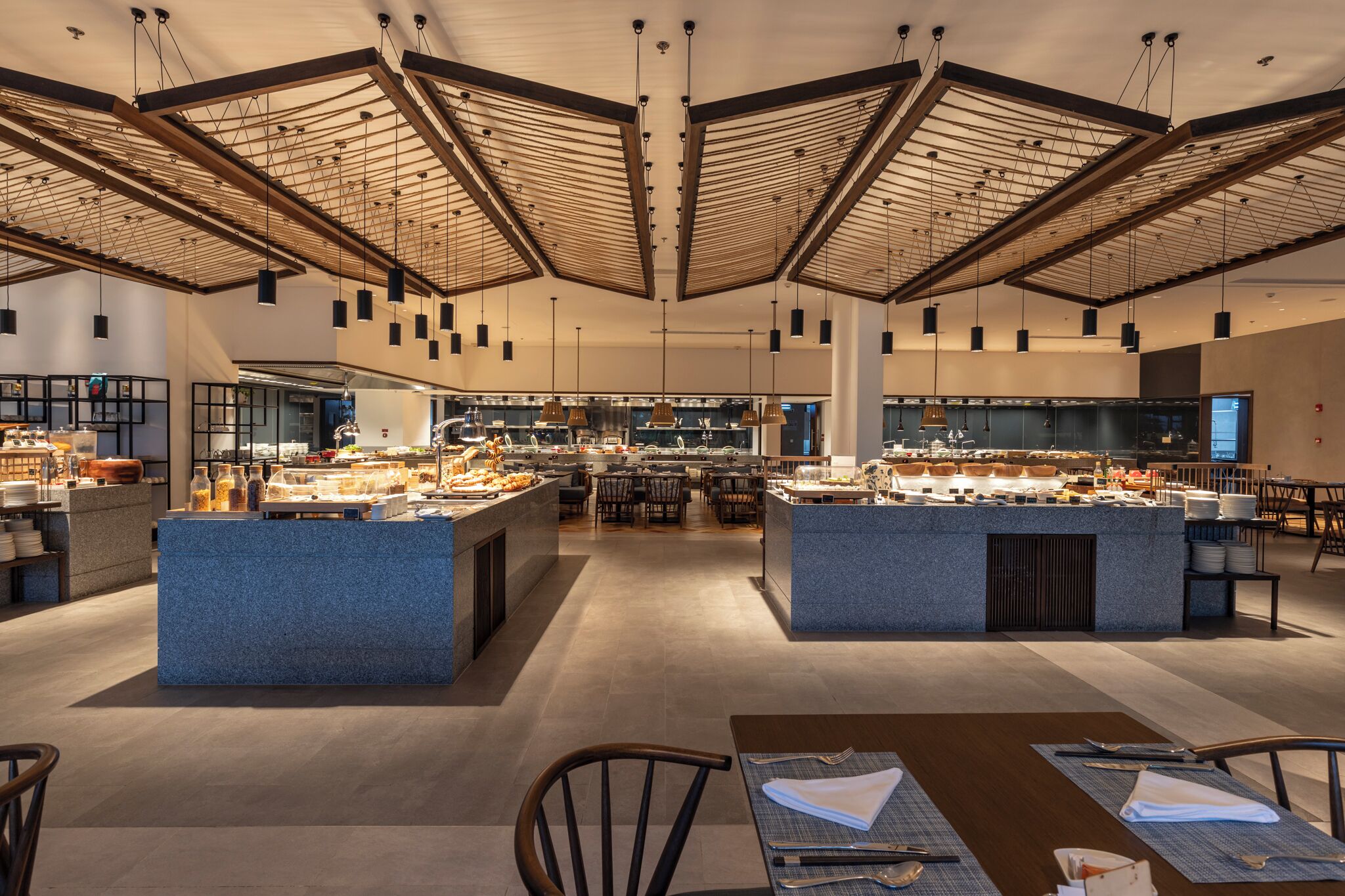 Un restaurante moderno con techos altos, iluminación colgante y una isla central con mostradores de comida.