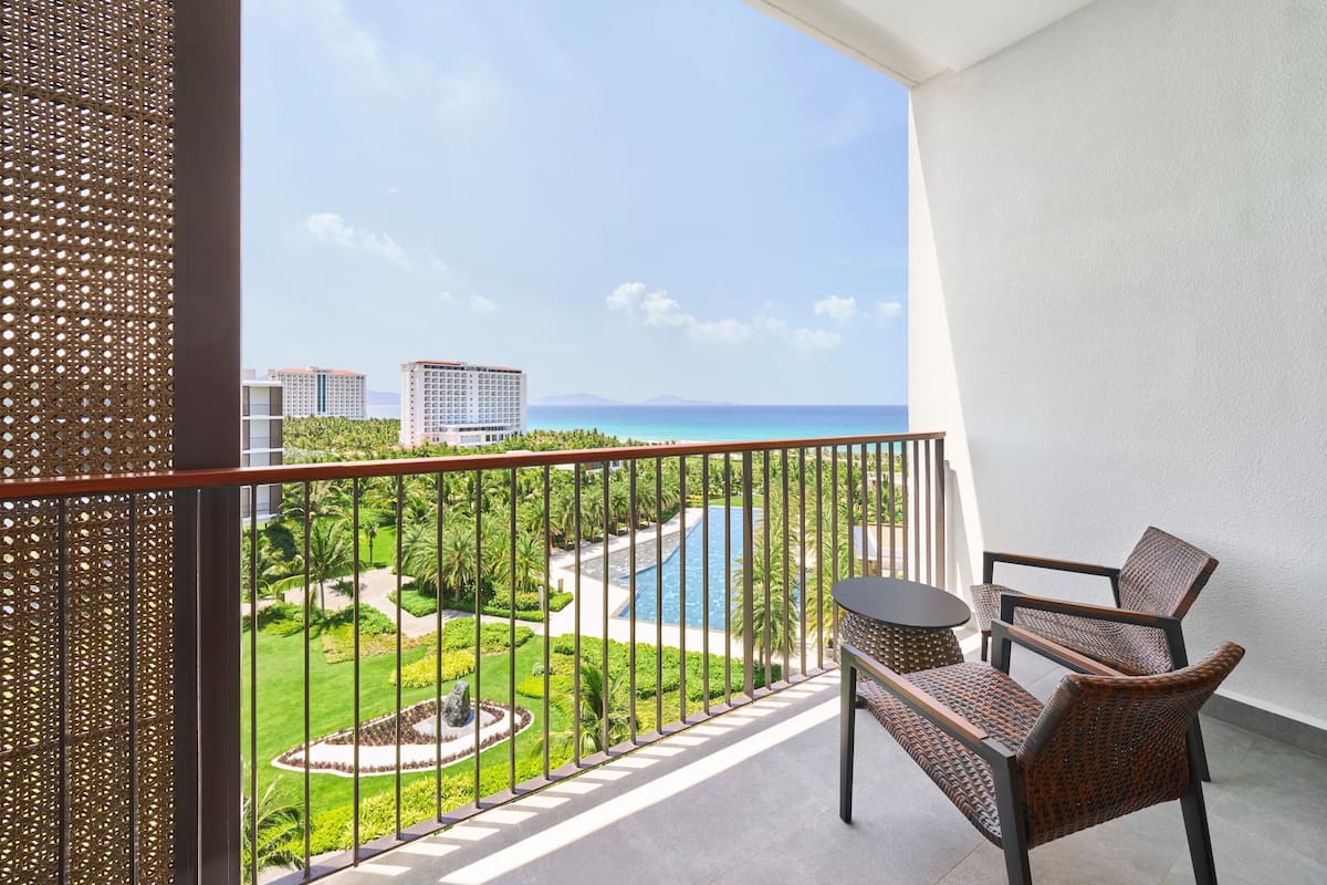 A balcony with wicker furniture, a pool, and a view of a resort area.