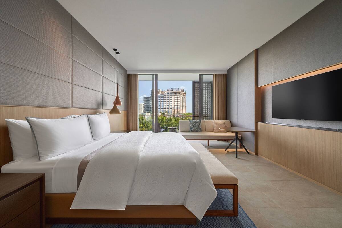 A modern hotel room with a large bed, a sofa, a TV, and a city view.