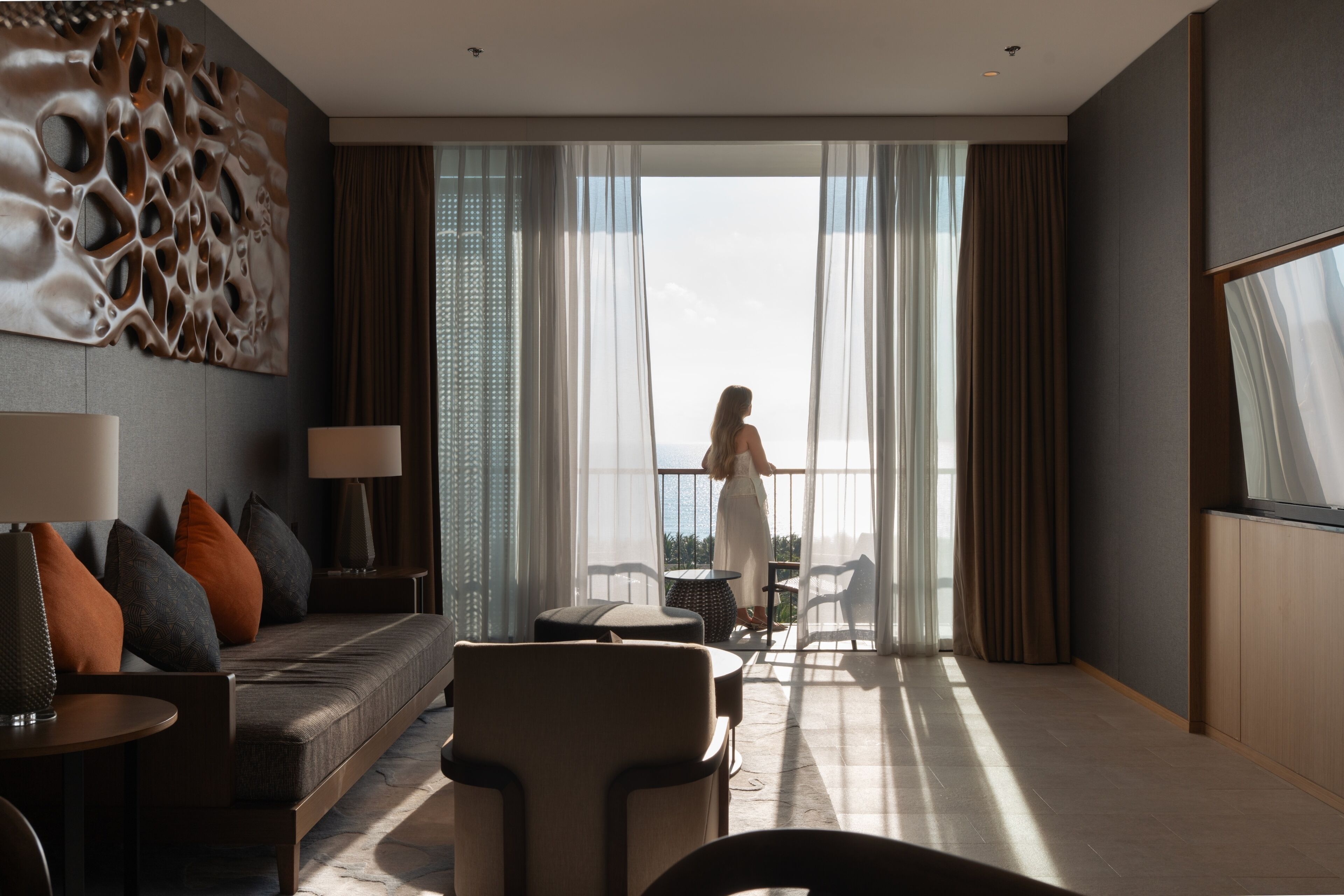 Una habitación de hotel moderna con un ventanal grande, un sofá, una mesa de comedor y un adorno de pared decorativo.