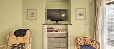 A living room with a television, wicker chairs, a storage unit, and a window with curtains.