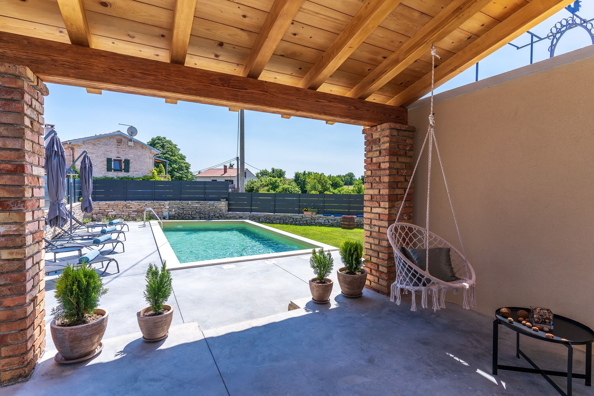 Eine Außenpatio mit Pool, Topfpflanzen, einem Hängesessel und Liegestühlen.