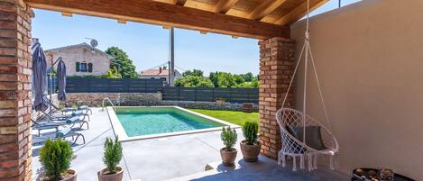 Eine Außenpatio mit Pool, Topfpflanzen, einem Hängesessel und Liegestühlen.