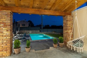 Un espace extérieur abrité comprenant une piscine, des plantes en pot et un fauteuil suspendu.