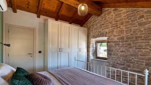Ein Schlafzimmer mit Steinwand, Holzboden und einem Bett mit Kissen sowie einem Kleiderschrank.