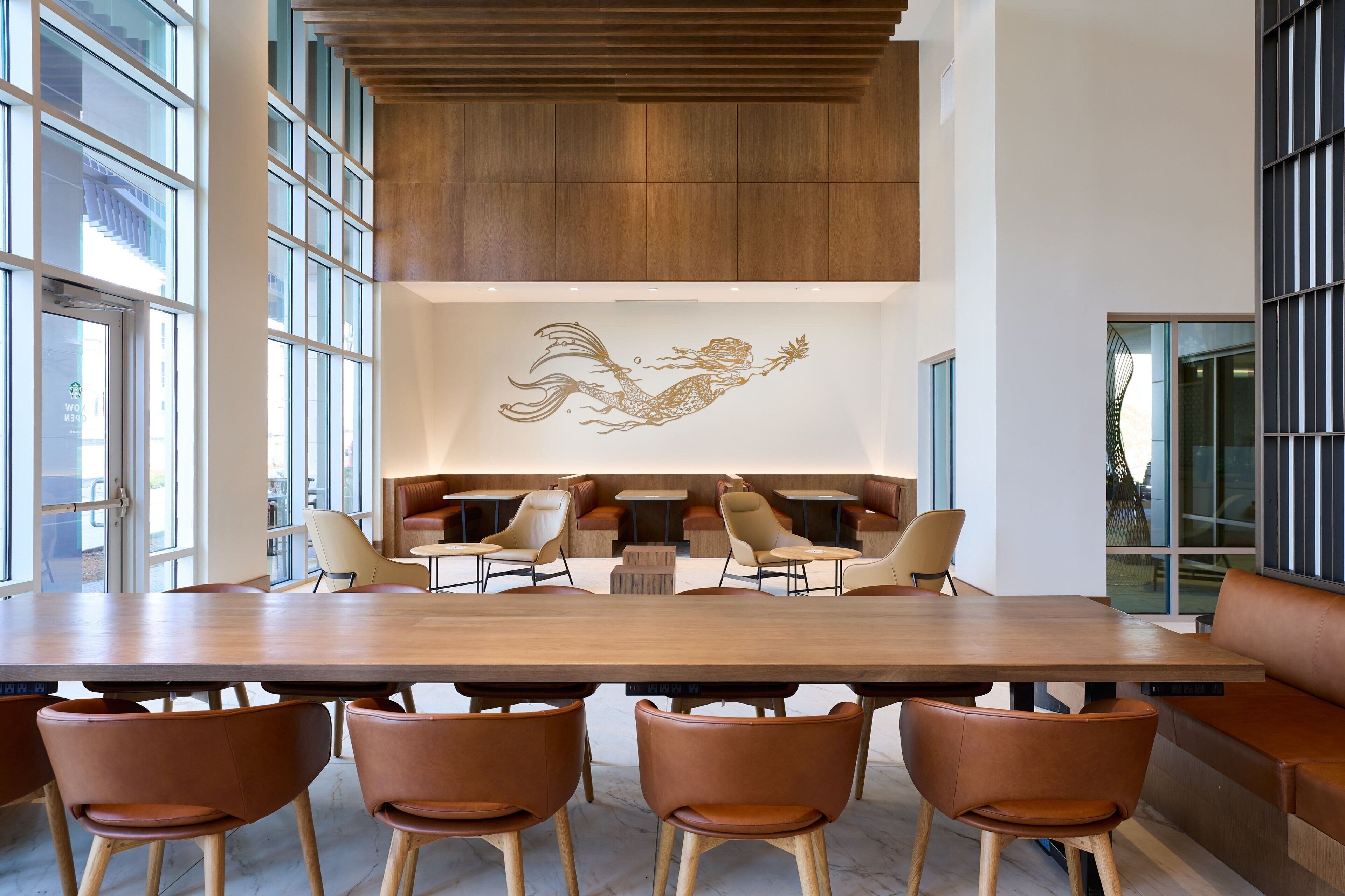 A spacious dining area with a long wooden table, brown leather chairs, and a mural of a mermaid on the wall.