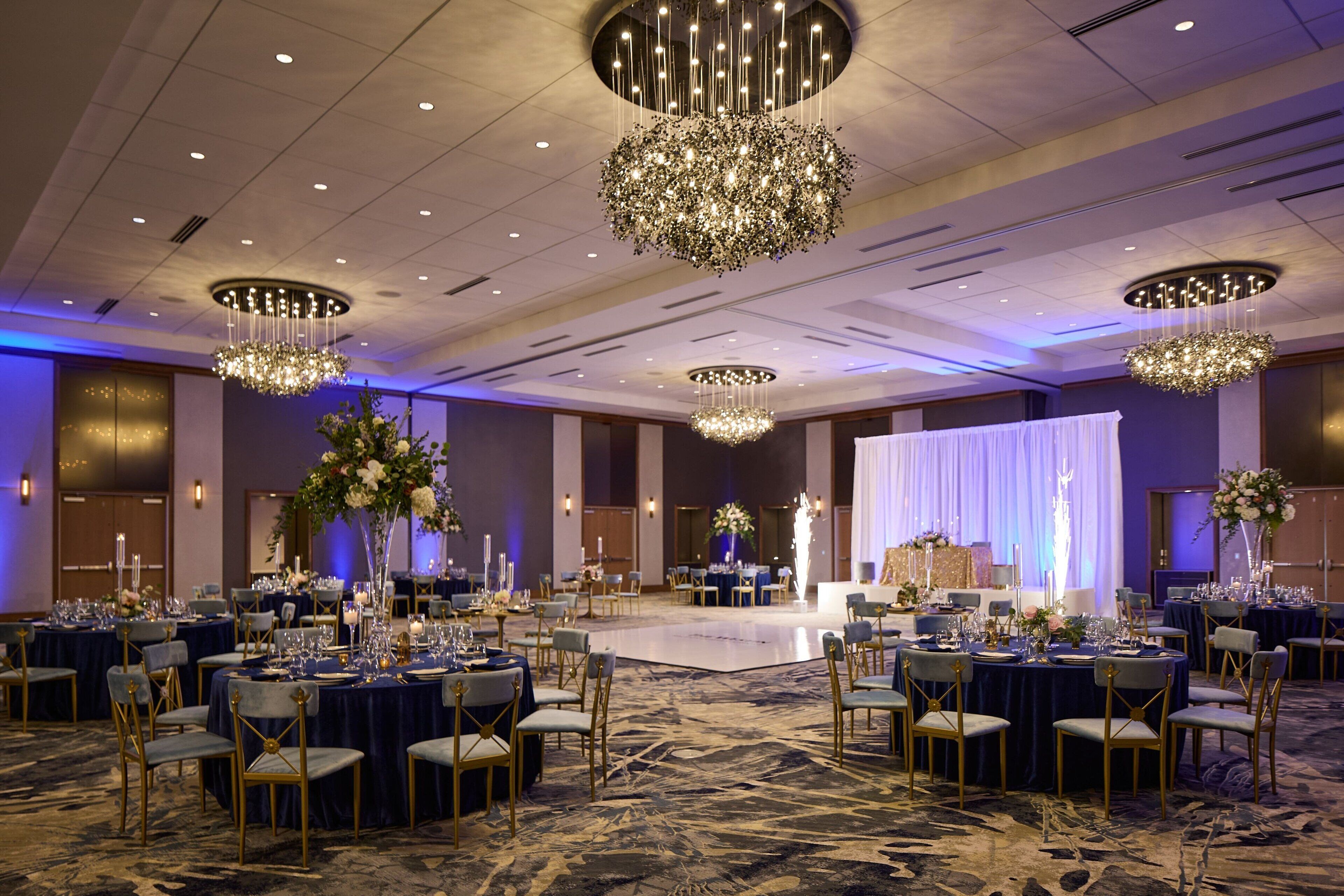 A banquet hall with round tables, chairs, and chandeliers.