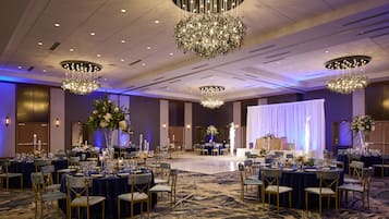 A banquet hall with round tables, chairs, and chandeliers.