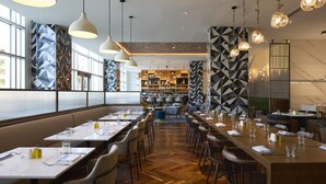 Un restaurante moderno con mesas comunes alargadas, lámparas colgantes y paredes con patrones geométricos.
