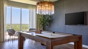 Una habitación moderna con mesa de billar, un ventanal con cortinas, una lámpara colgante y un televisor de pantalla plana montado en la pared.