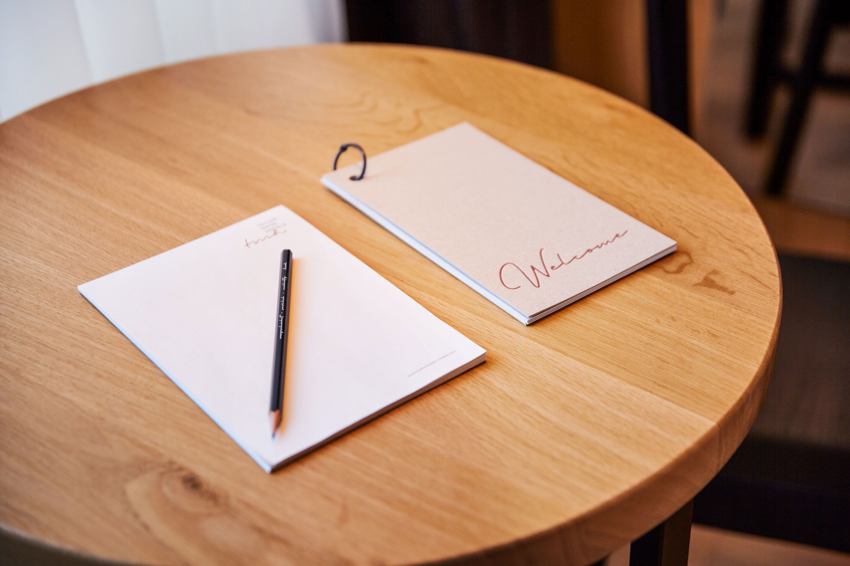 A wooden table with two white notepads and a pen.