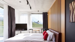 Une chambre d’hôtel moderne, dotée d’un grand lit, d’une télévision, d’une petite table et offrant une vue sur l’extérieur.