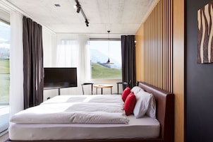 Una habitación de hotel moderna con una cama grande, un televisor, una mesita y vistas al exterior.
