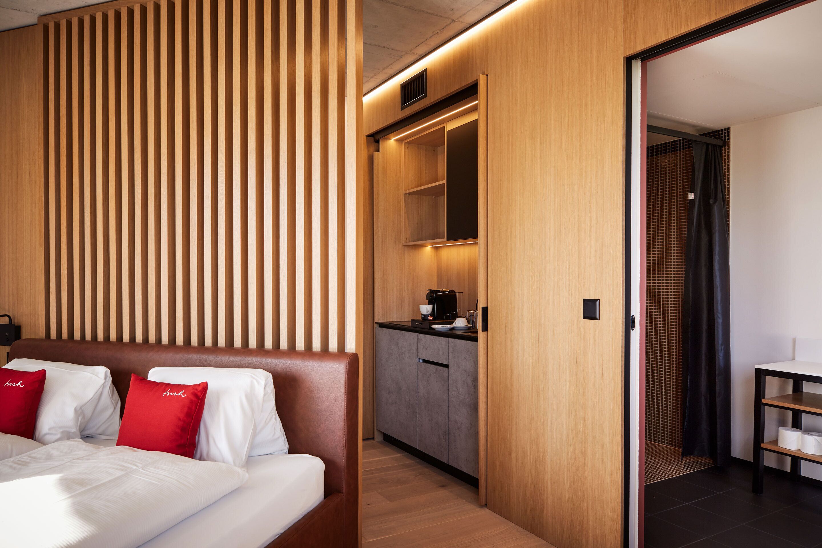 Une chambre d’hôtel comprenant un lit, un mur recouvert de panneaux en bois, une kitchenette et un espace douche.