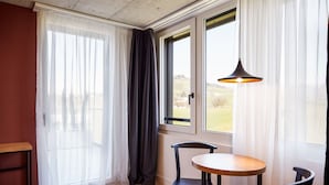 Une pièce avec une table et des chaises en bois, une fenêtre avec des rideaux et un luminaire suspendu.