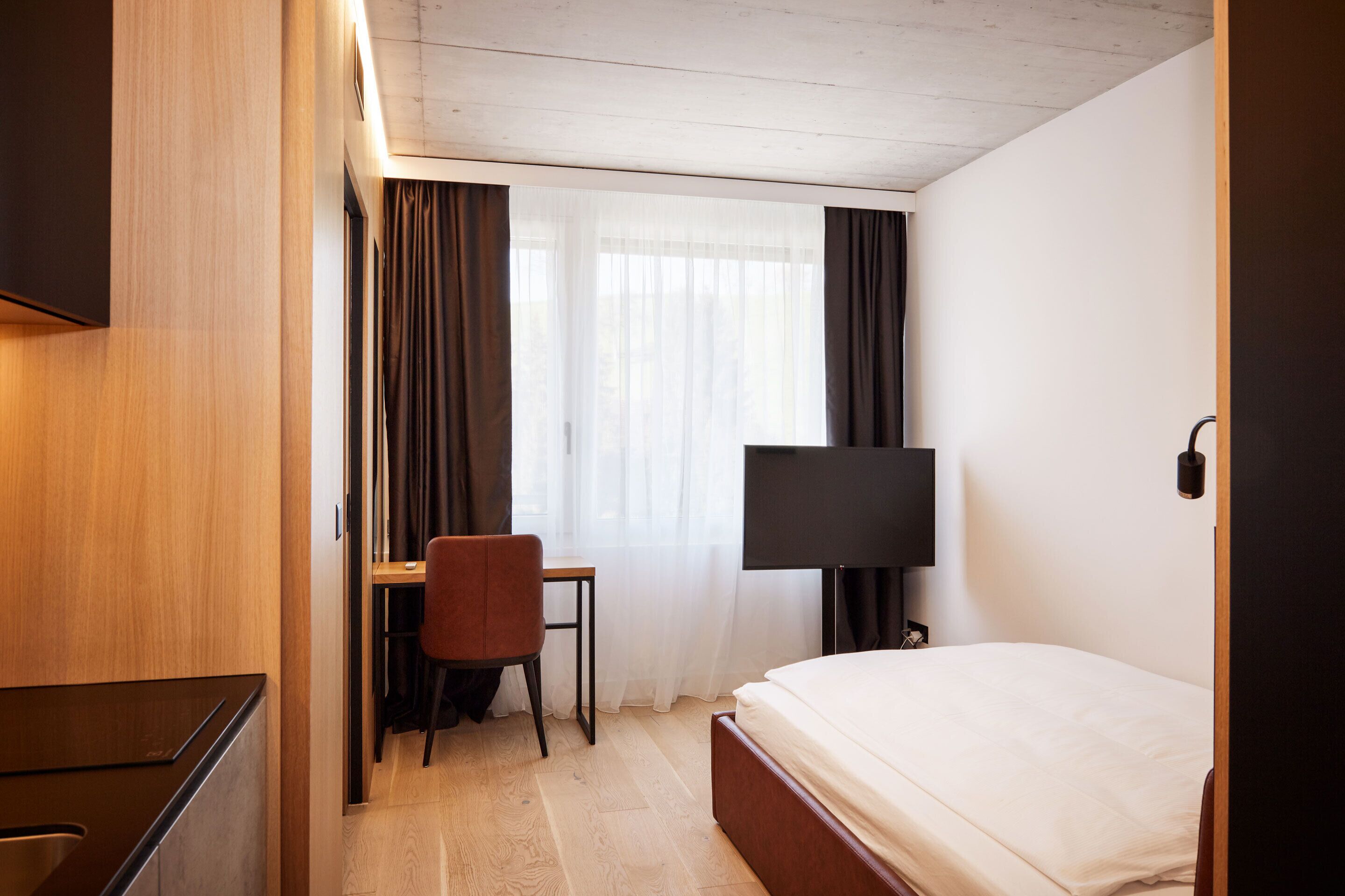 Een hotelkamer met een bed, een bureau, een stoel, een televisie en een raam met gordijnen.
