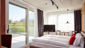 Une chambre d’hôtel avec un grand lit, une télévision, une petite table et une vue sur un paysage verdoyant.