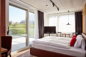 Habitación de hotel con una cama grande, un televisor, una mesita y vistas a un paisaje verde.