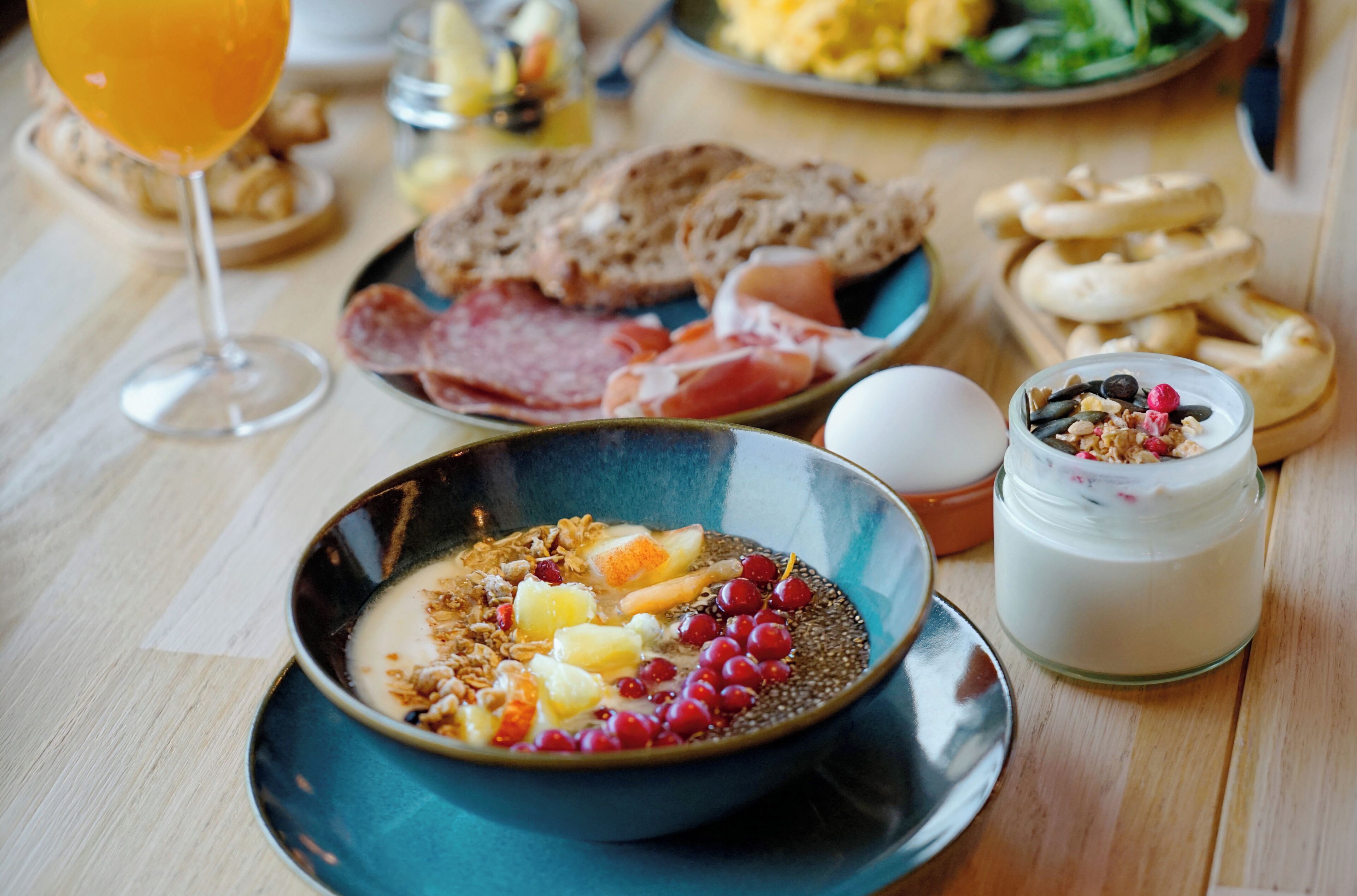 Ein Frühstückstisch mit einer Schüssel Müsli, einem Glas Orangensaft und verschiedenen Backwaren.