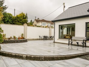 A patio with a tiled floor, a seating area with chairs and a table, and a white wall with a window. - Wee Andy's (Buncrana)