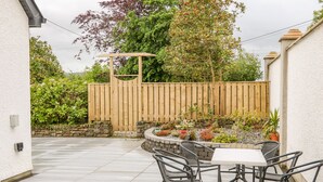 A patio with a table and chairs, surrounded by a stone wall and various plants. - Wee Andy's (Buncrana)