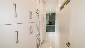 A modern kitchen with white cabinets, a built-in oven, and a washing machine. - Wee Andy's (Buncrana)