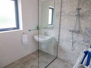 A modern bathroom with a glass shower enclosure, a white sink, and a glass shelf above the sink. - Wee Andy's (Buncrana)