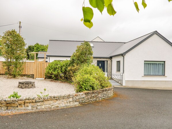 A residential property with a stone retaining wall, a wooden fence, and a house with a white exterior and a dark door. - Wee Andy's (Buncrana)