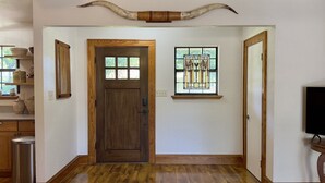 A hallway with a wooden door, a stained glass window, and a large horn decoration above the door. - Sunnyside | Fire Pit | Spacious & Comfortable (Fredericksburg)