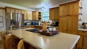 A kitchen with wooden cabinets, stainless steel appliances, a central island, and a dining area with chairs. - Sunnyside | Fire Pit | Spacious & Comfortable (Fredericksburg)