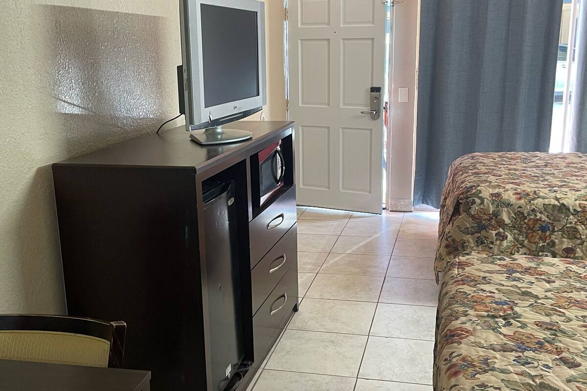 Une chambre avec un lit, un bureau avec une télévision, un four à micro-ondes et une porte.
