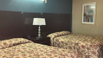Una habitación de hotel con dos camas, una mesita de noche con lámpara, un cuadro enmarcado en la pared y una pared azul con textura.
