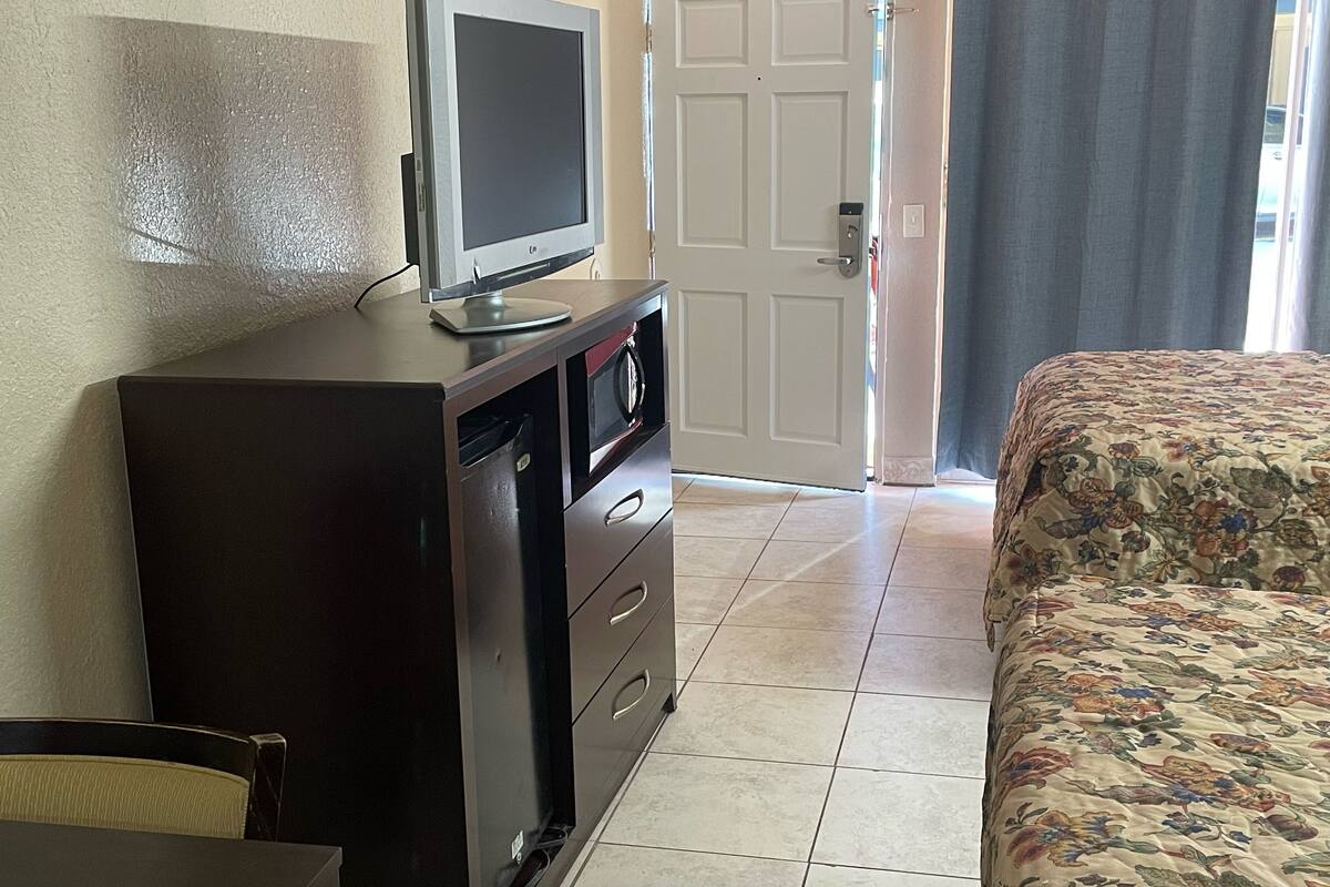 Une chambre d’hôtel avec un lit, un bureau avec une télévision, un four à micro-ondes et une porte.