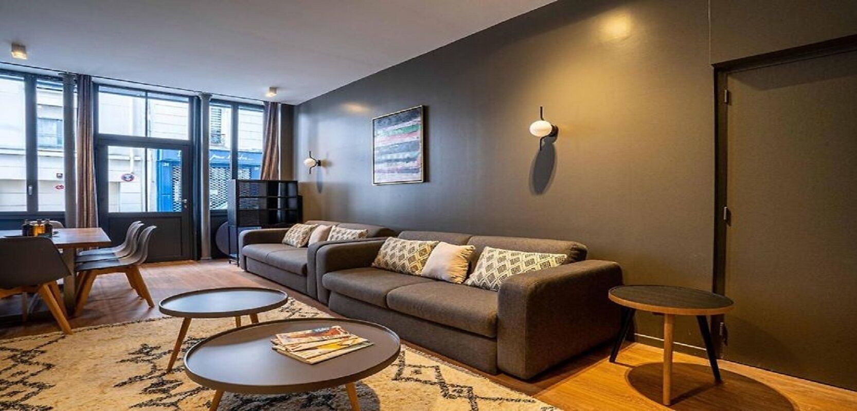 A modern living room with a sofa, two coffee tables, and a dining area with chairs and a table.