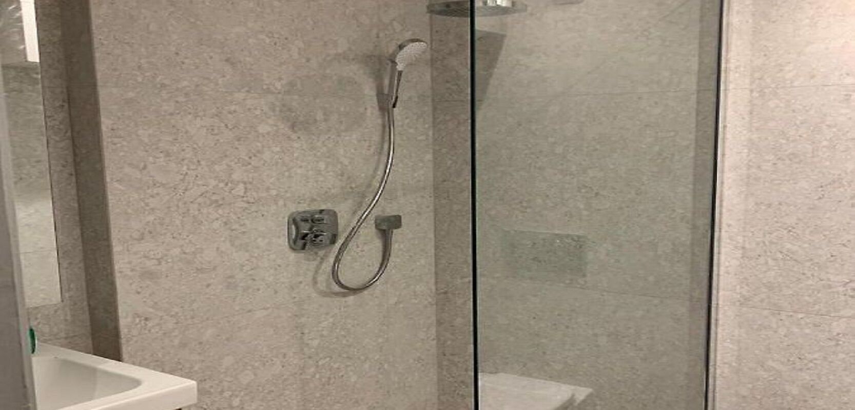 A shower with a glass door, a wall-mounted control panel, and a white sink.