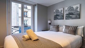 Una habitación de hotel con una cama grande, dos lámparas fijadas a la pared y dos cuadros enmarcados.