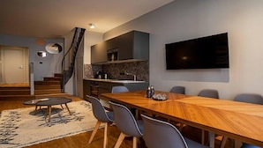 Una sala de estar moderna con una mesa de comedor de madera, sillas grises, un televisor montado en la pared y una escalera que sube a un nivel superior.