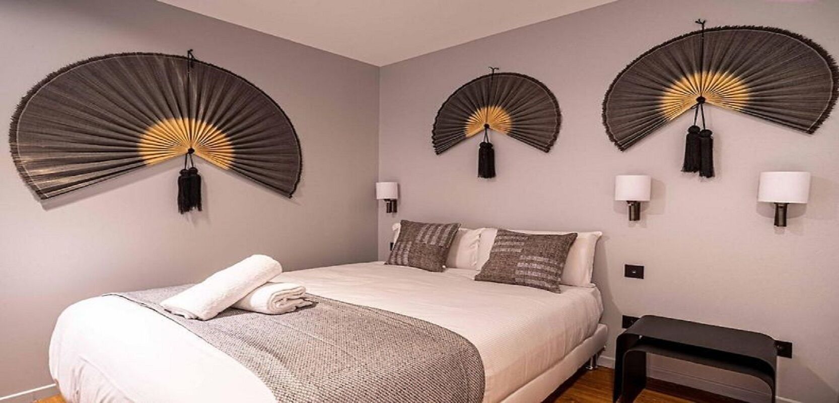 Une chambre à coucher avec un lit, trois ventilateurs fixés au mur, deux lampes de chevet et une petite table.