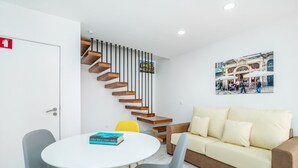 Un interior moderno con una mesa redonda blanca, dos sillas, un sofá y una escalera de madera.