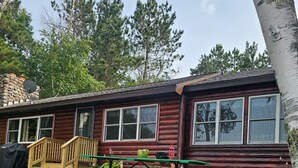 A log cabin with a deck, a picnic table, and a stone fireplace.