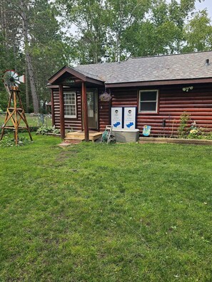 A rustic log cabin with a small porch and a windmill in the yard.